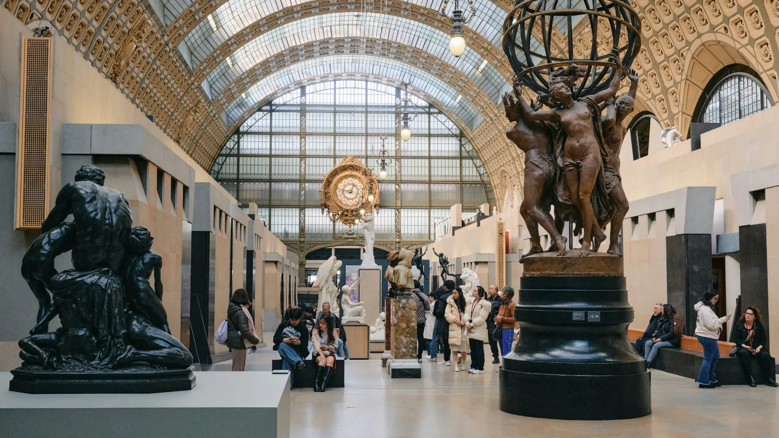 Interior of Musée d'Orsay with sculptures, visitors, and a prominent glass ceiling.