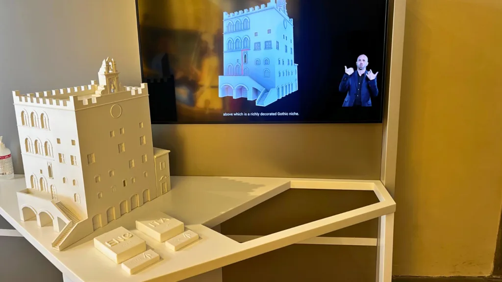 White 3D-printed architectural model with Gothic features next to a screen showing a digital version on video with a sign language interpreter and captions.