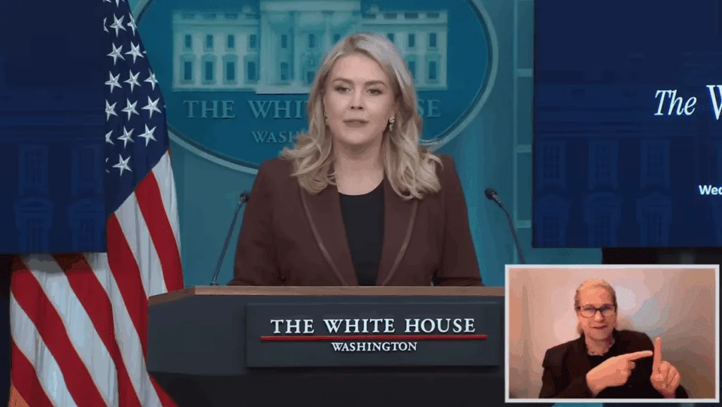 A speaker at a White House podium with an American flag and a sign language interpreter inset.