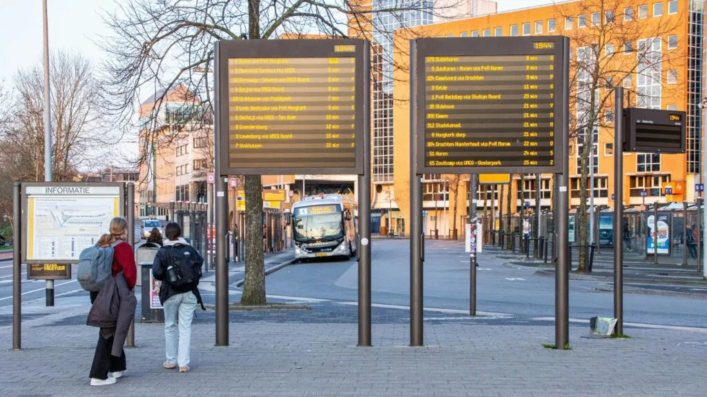 Bus terminal with electronic schedule boards and a parked bus in an urban area. 