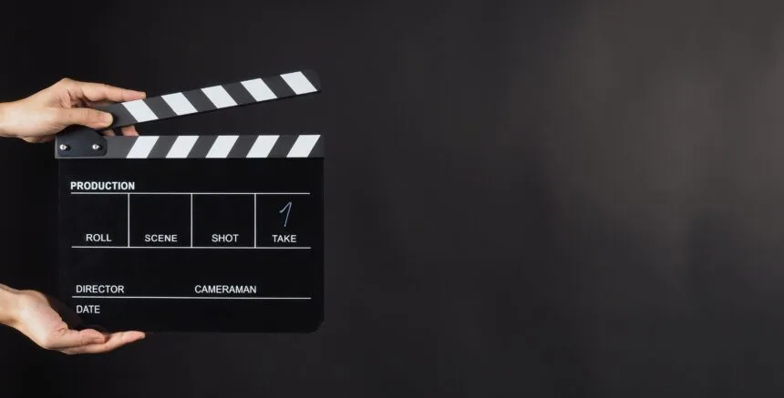 Hand is holding Black clapperboard or movie slate on black background.