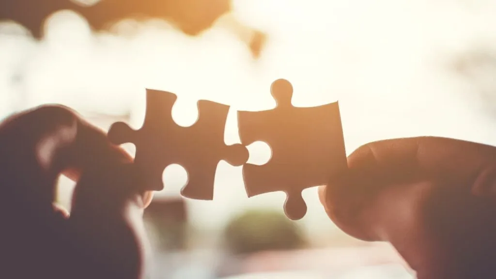 Two hands holding matching puzzle pieces against a bright, glowing background.