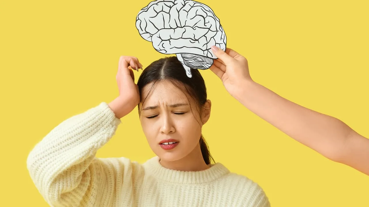 Person wincing with a drawing of a brain being held above their head against a yellow background.